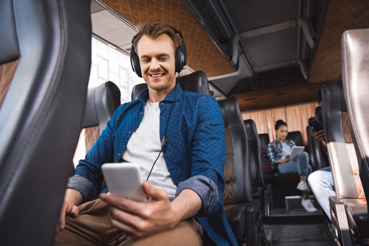 happy-adult-man-in-headphones-listening-music-and-using-smartphone-during-trip-on-bus.jpg